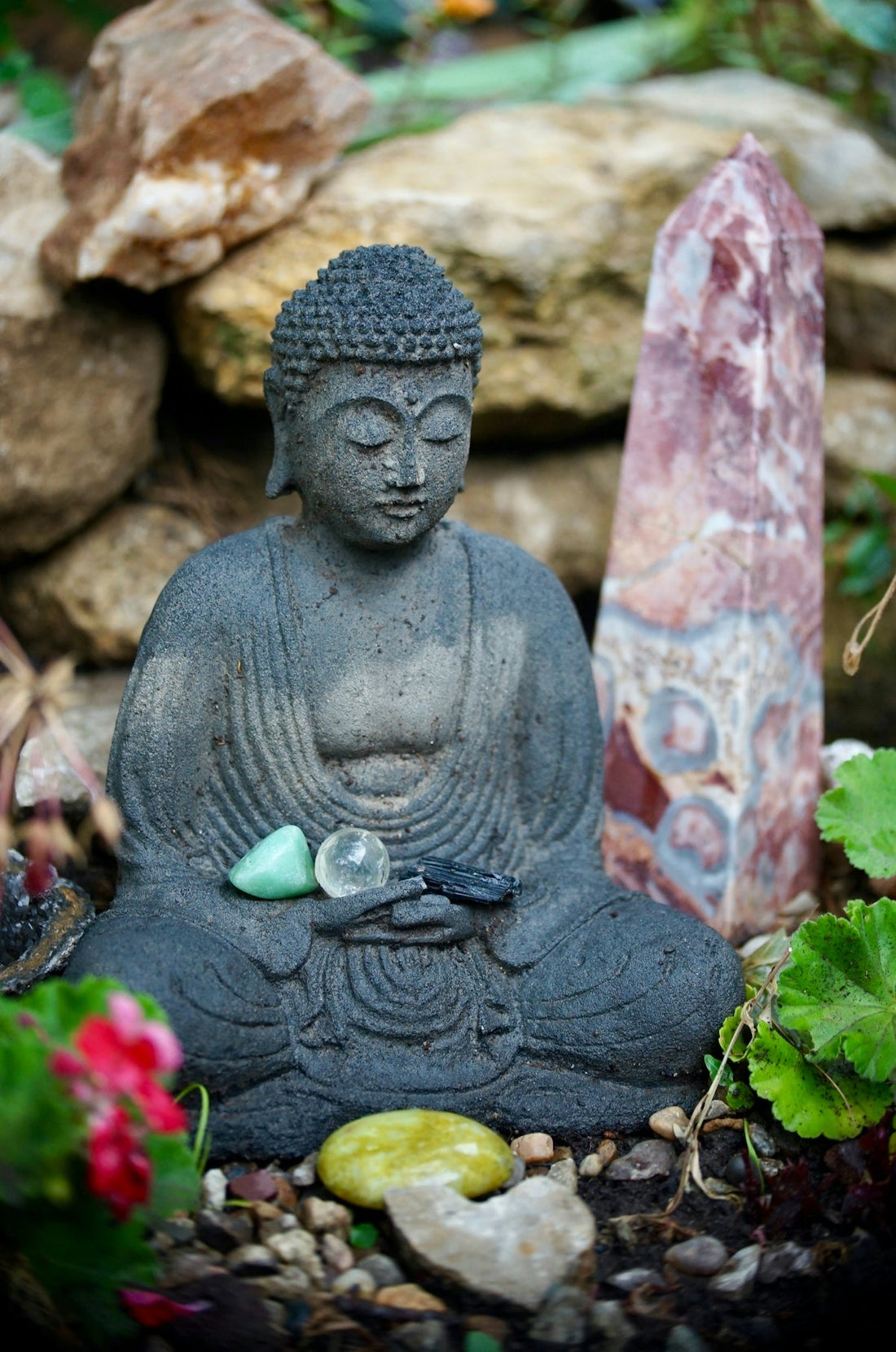 Stone buddha statue with crystals in a garden setting.
