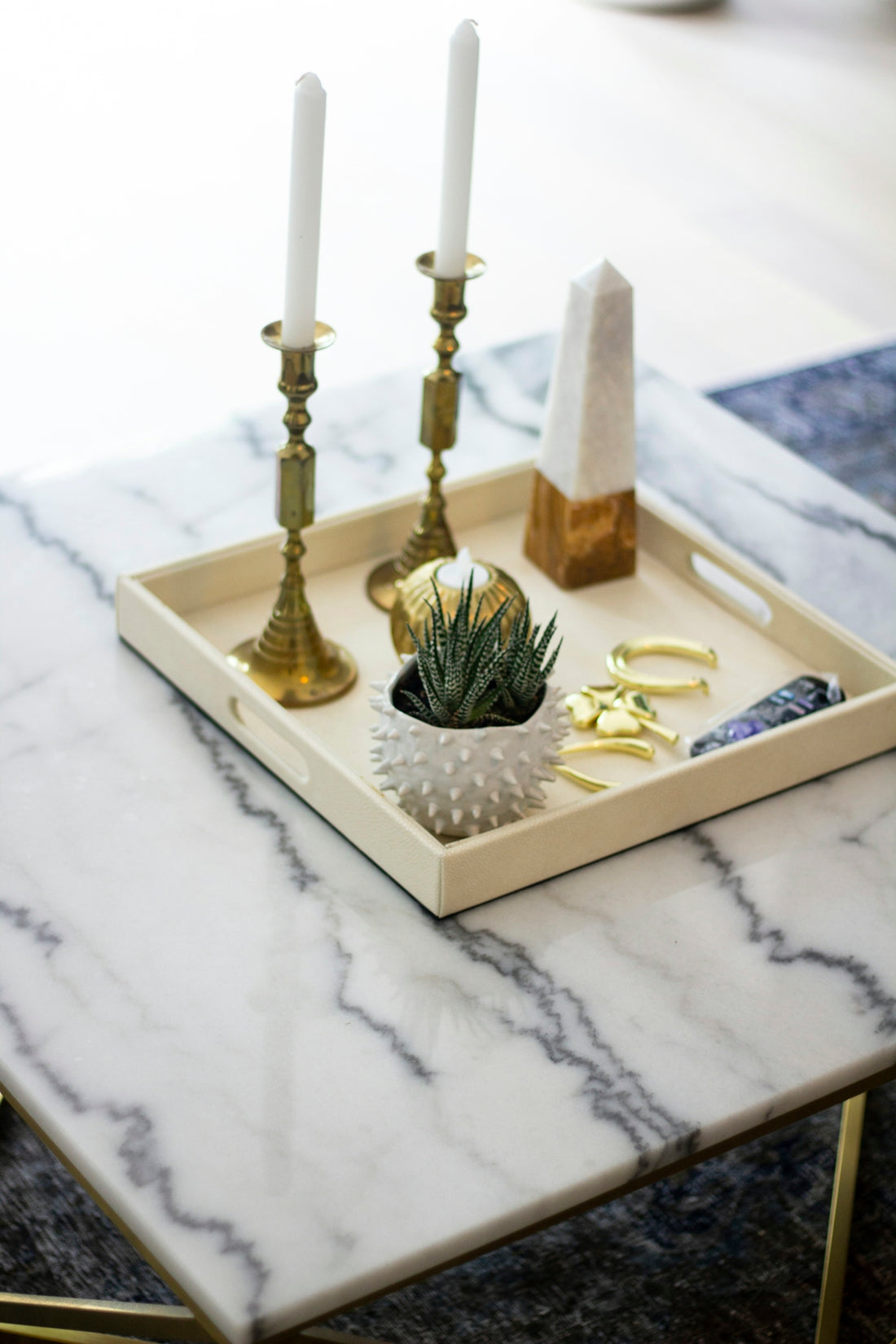 Decorative tray with candles, plant, and crystals on table.