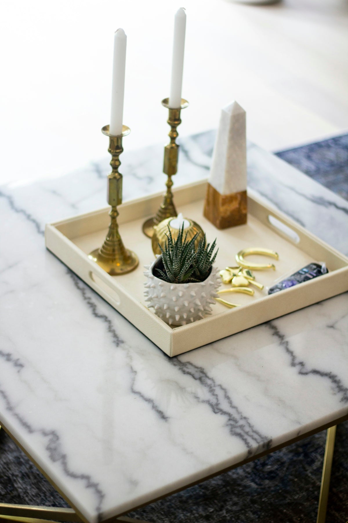 Decorative tray with candles, plant, and crystals on table.
